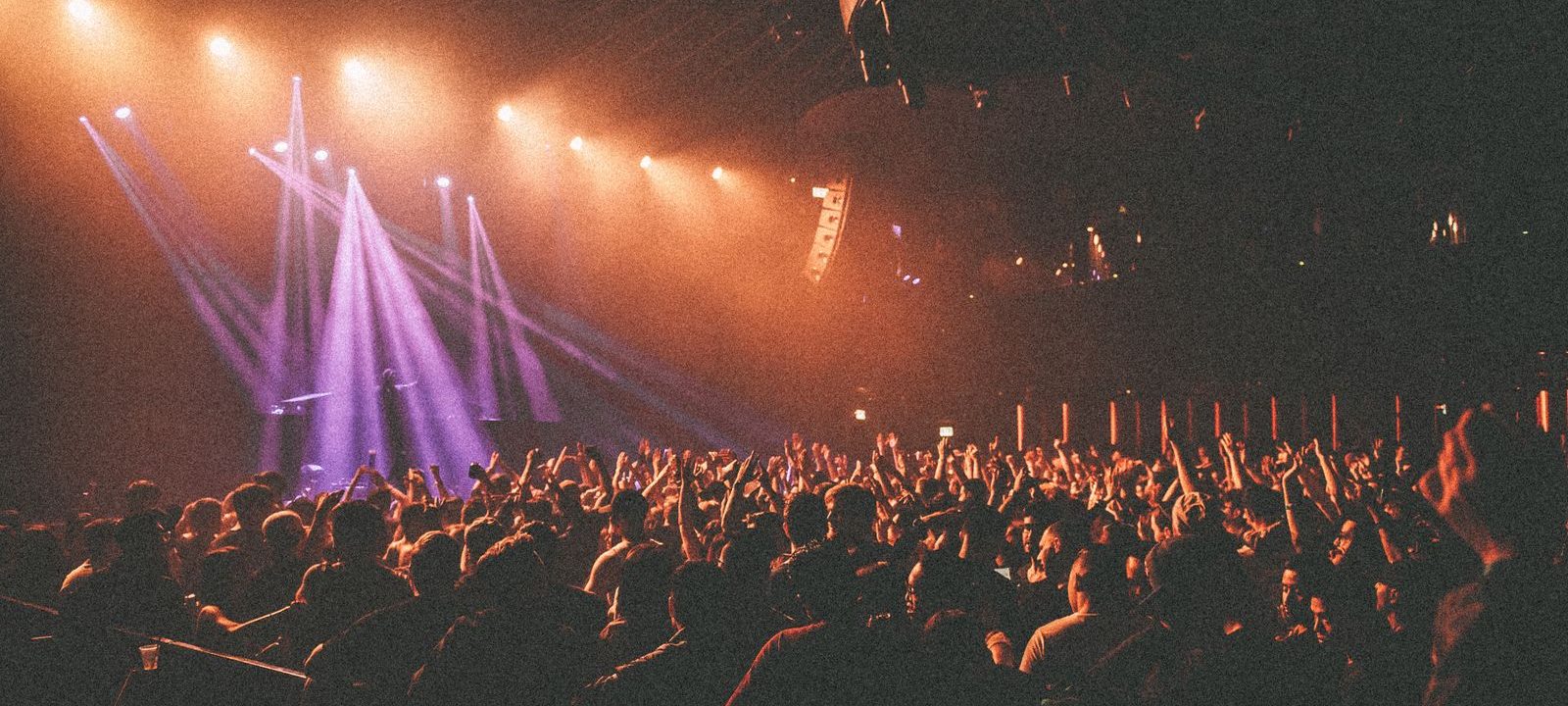 A packed club crowd with hands raised under warm orange stage lights