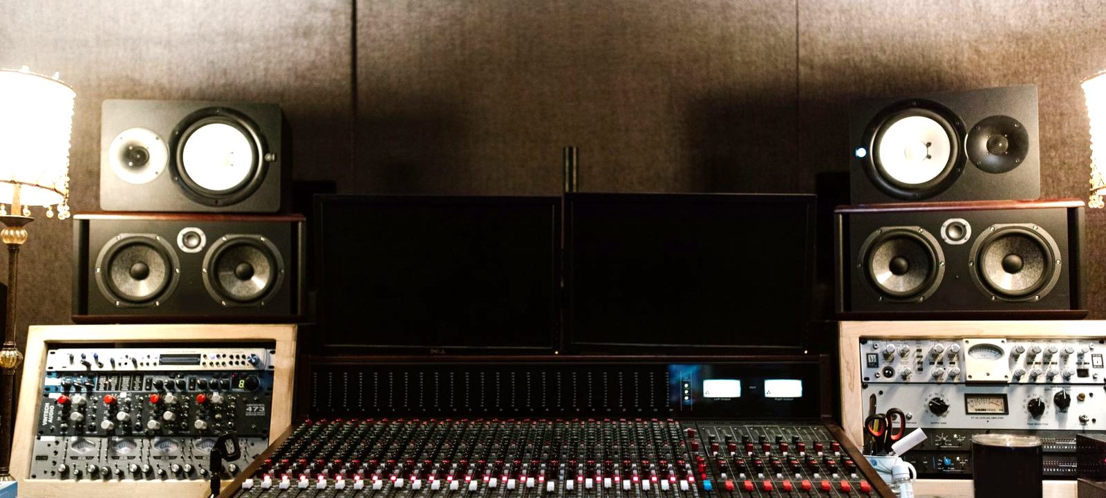 Studio monitor speakers positioned on stands either side of a mixing console in a treated room