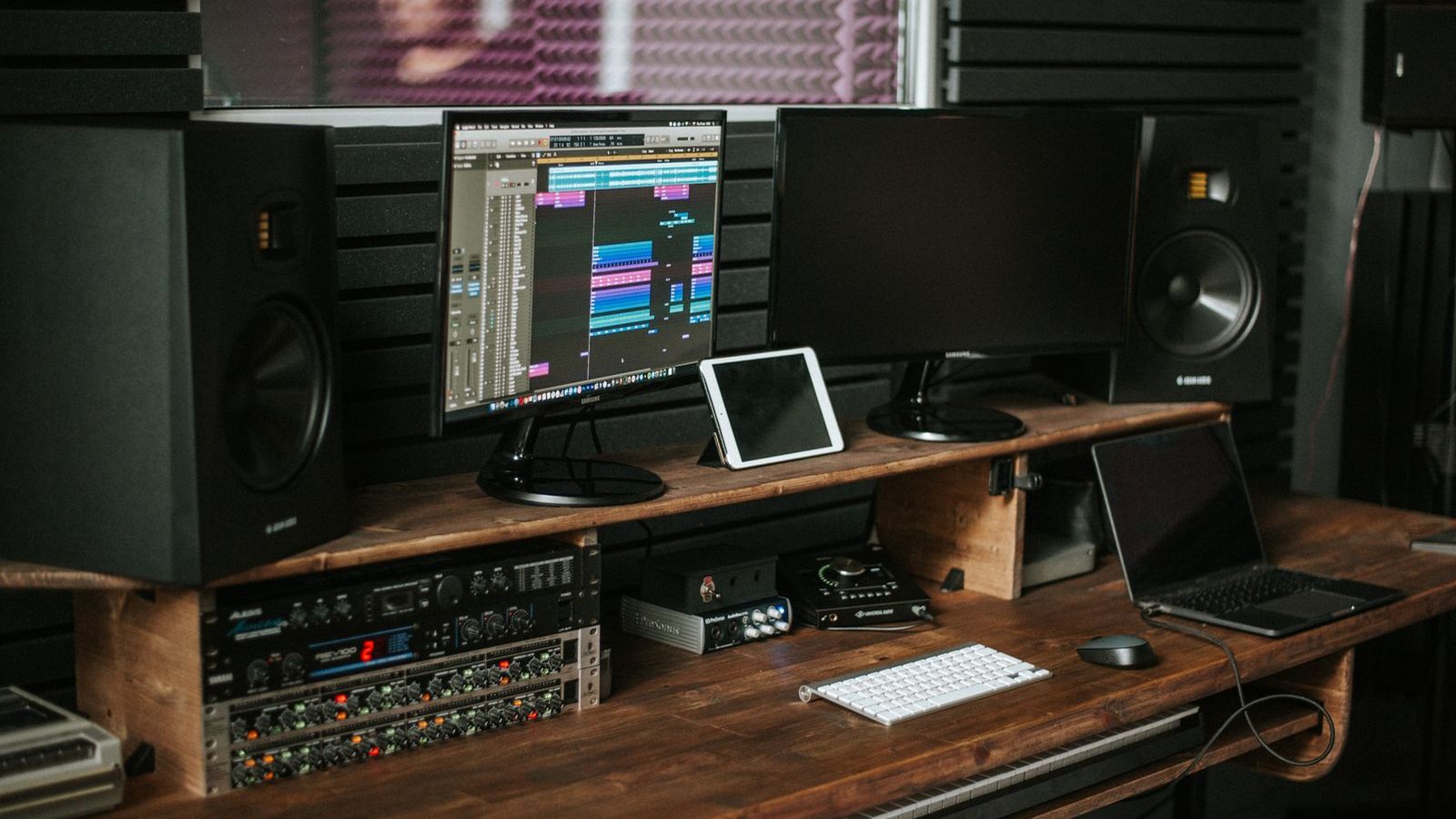 A pair of studio monitor speakers set up either side of a producer's desk in a warm-lit studio